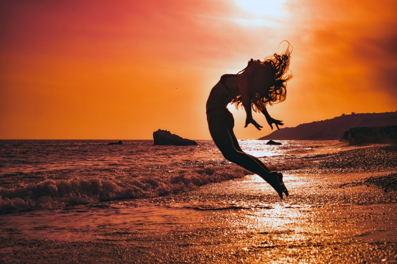Young woman jumping on the shore in the sunset