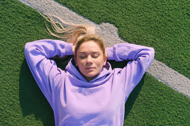 A young blonde woman wearing a hoodie while lying on the pitch