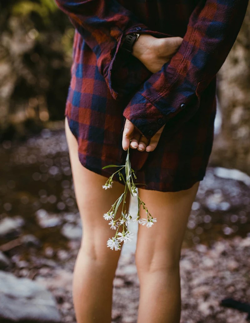 A woman in a flannel shirt holding flowers behind her back