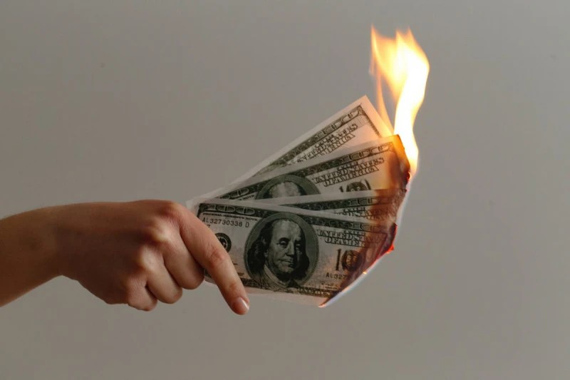 A hand holding a burning $100 notes